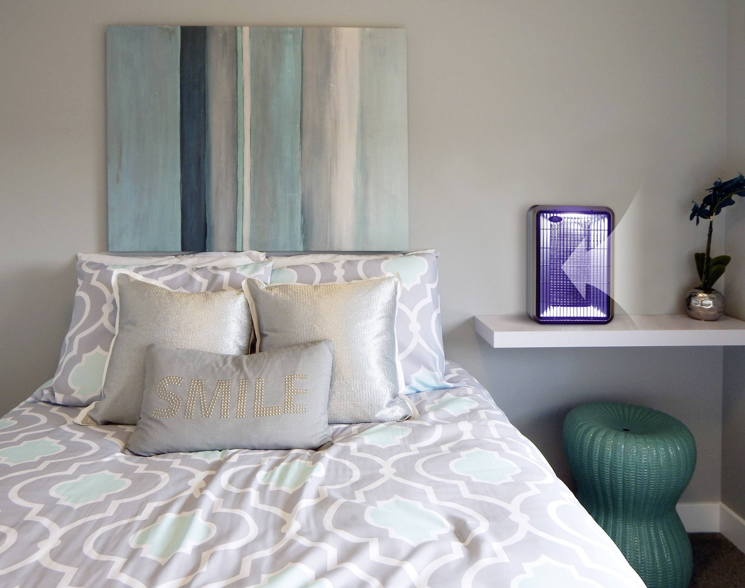 Gezellige slaapkamer met een bed in blauw- en grijstinten, decoratieve kussens en een kunstwerk aan de muur. Rechts een bijzettafel met een plant.