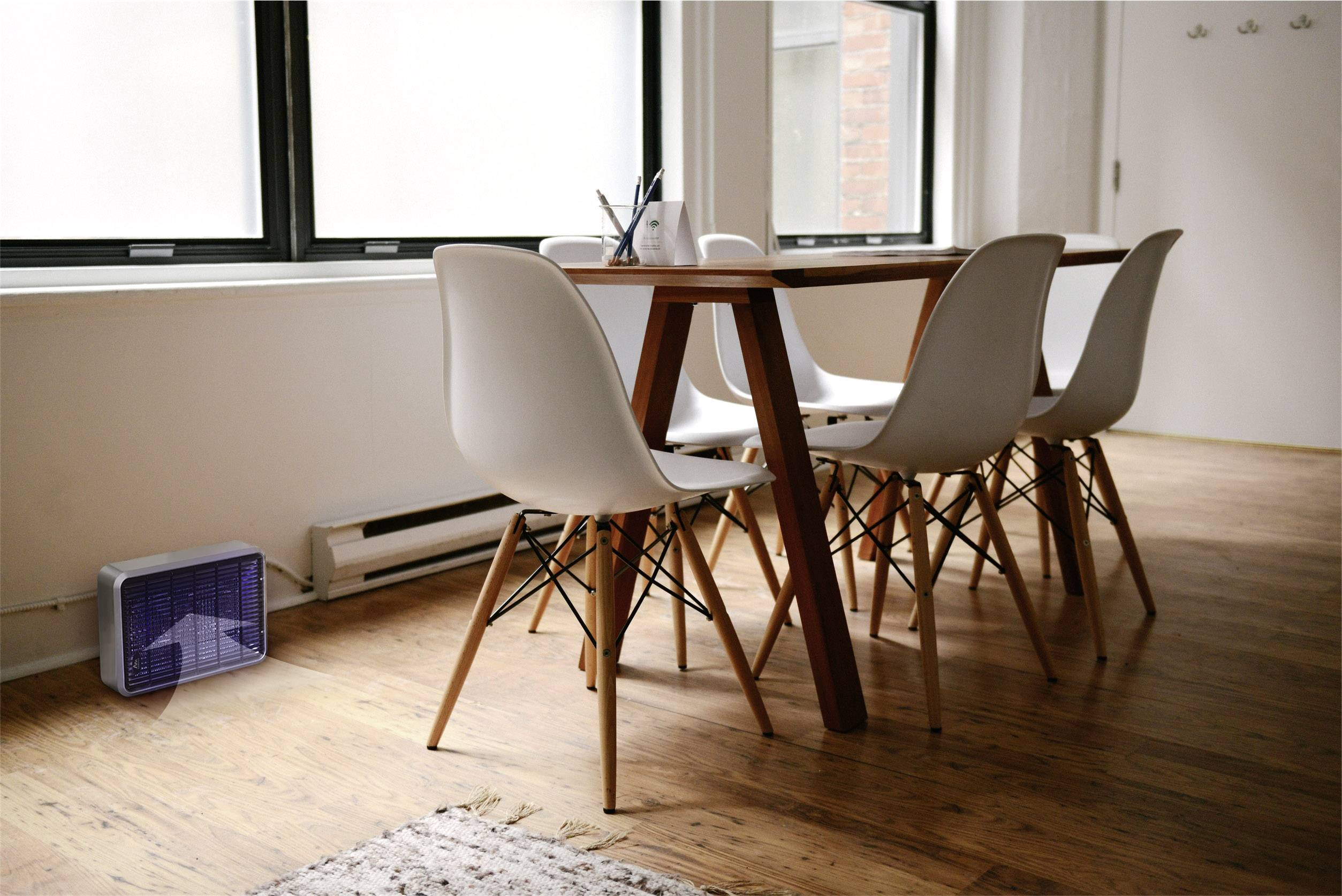 Een moderne eetruimte met een tafel en vier witte stoelen op een houten vloer. Naast de tafel staat een luchtontvochter.