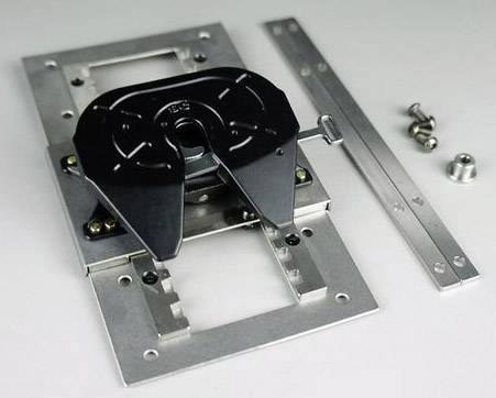 Metalen slee met zwart, verstelbaar gewricht, geflankeerd door schroeven en metalen strips op een grijze ondergrond.