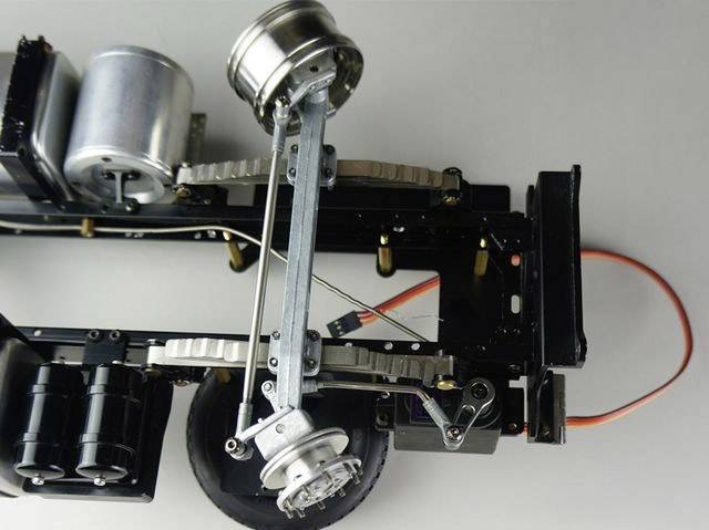 Modelauto-chassis van metaal met zichtbare elektronica en bekabelde motor. De voorste as is te zien zonder carrosserie.