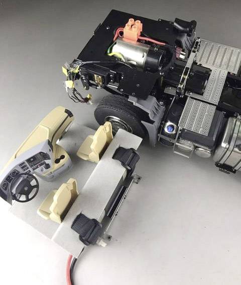 Model van een auto met gedeeltelijk zichtbare binnenruimte. Technische componenten zoals motor en kabels met panoramisch beeld van het dashboard.