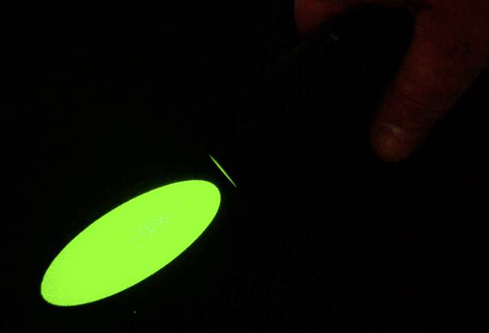Een hand houdt een zwarte zaklamp vast, die een felgroene lichtstraal projecteert op een donkere achtergrond.