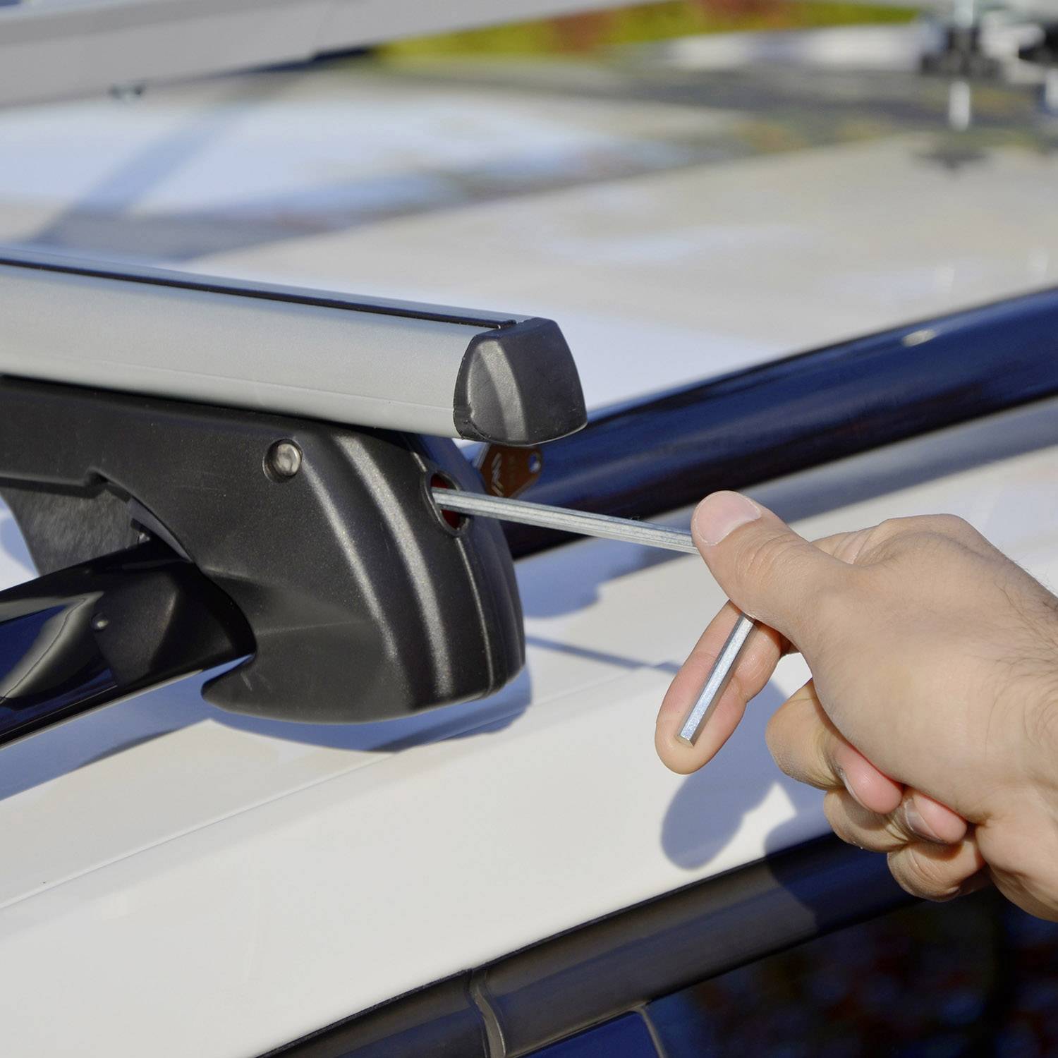 Een hand trekt een gereedschapshendel aan een dakdragerbevestiging van een auto. Focus op de hand en de hendel, achtergrond wazig.
