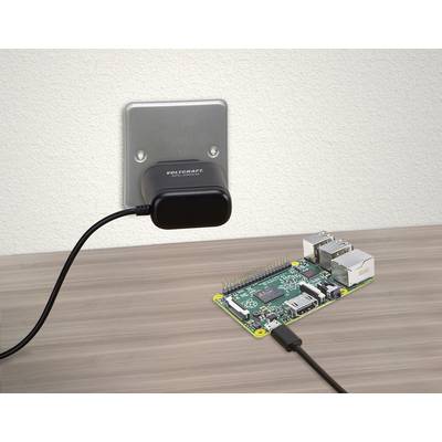 Een oplader is in een stopcontact gestoken en verbonden met een kleine computer, zoals een Raspberry Pi, op een tafel.