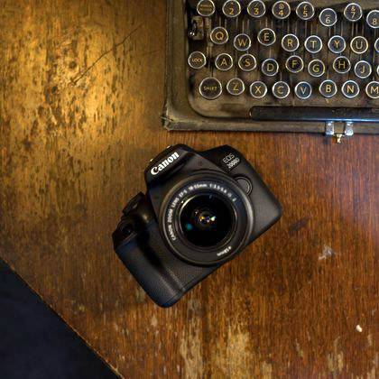 Een oude typemachine en een moderne camera liggen naast elkaar op een houten tafel, symboliseren de verandering van technologie.