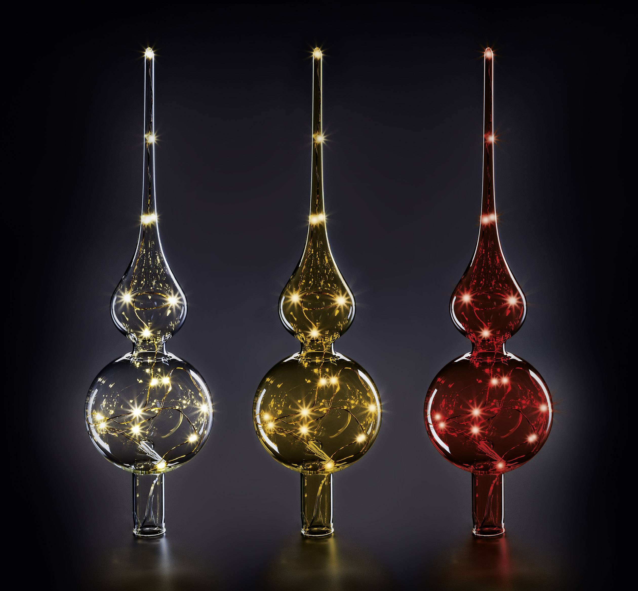 Drie glazen kerstboompieken in zilver, goud en rood, verlicht en fonkelend, staan naast elkaar op een donkere achtergrond.