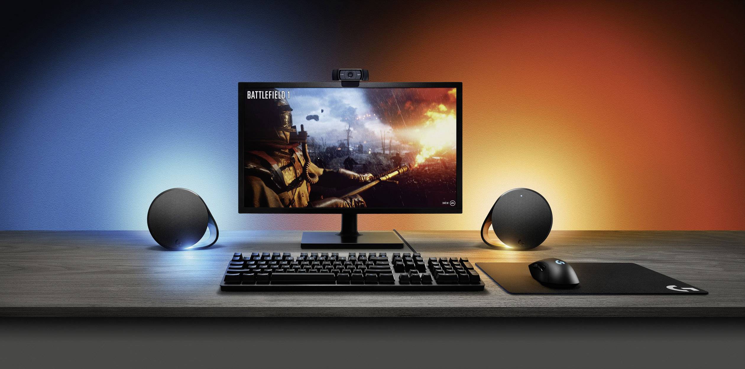 Computerworkstation met monitor waarop een oorlogsspel wordt gespeeld. Gaming-toetsenbord en -muis op tafel. Achtergrondverlichting in blauw en oranje.