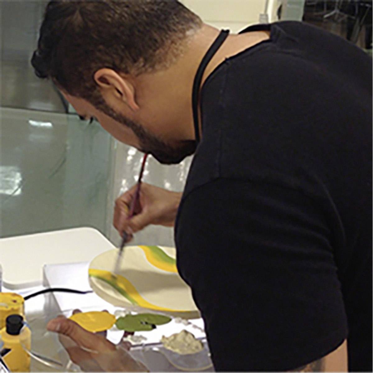 Een man schildert met een penseel op een wit doek in een atelier. Hij gebruikt geel- en groentinten.