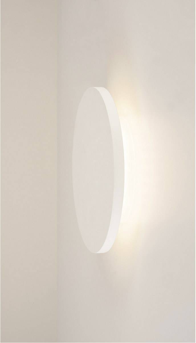 Witte, ronde wandlamp aan een beige muur, die zacht licht uitstraalt.