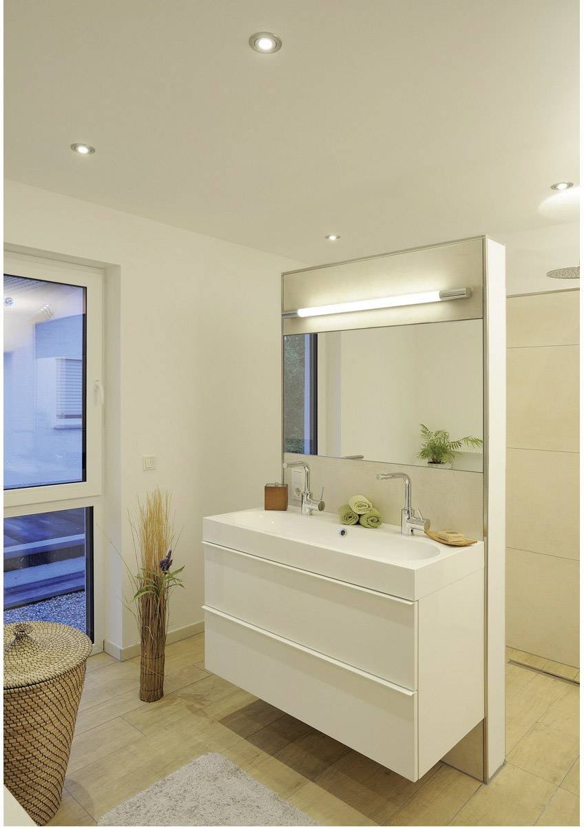 Modern badkamer met verlichte spiegel boven de wastafel, links een raam, rechts een douche. Lichte houten vloer, subtiele planten.