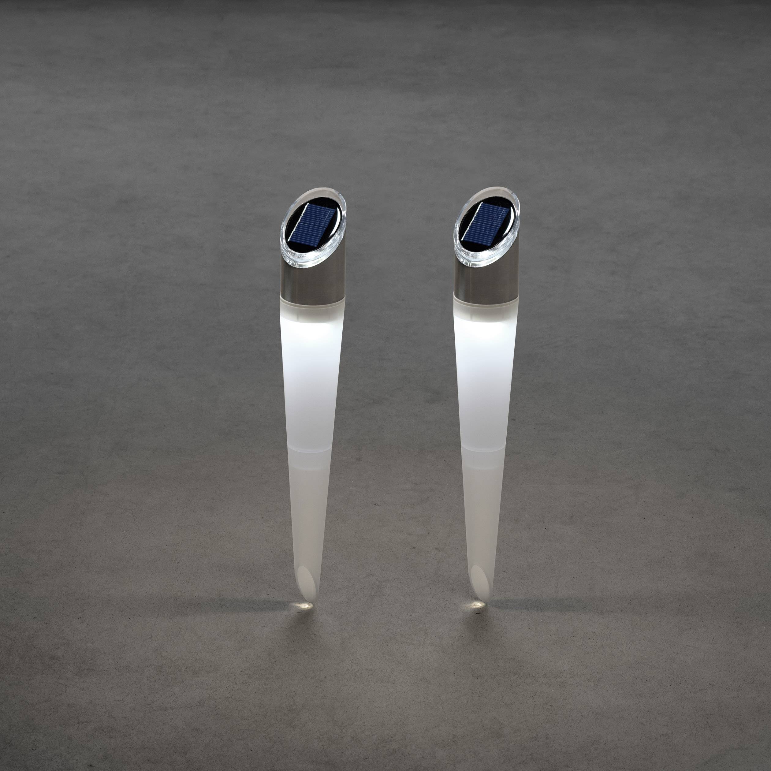 Twee slanke, op zonne-energie werkende tuinlampen met een kegelvormig ontwerp schijnen op een donkere ondergrond.