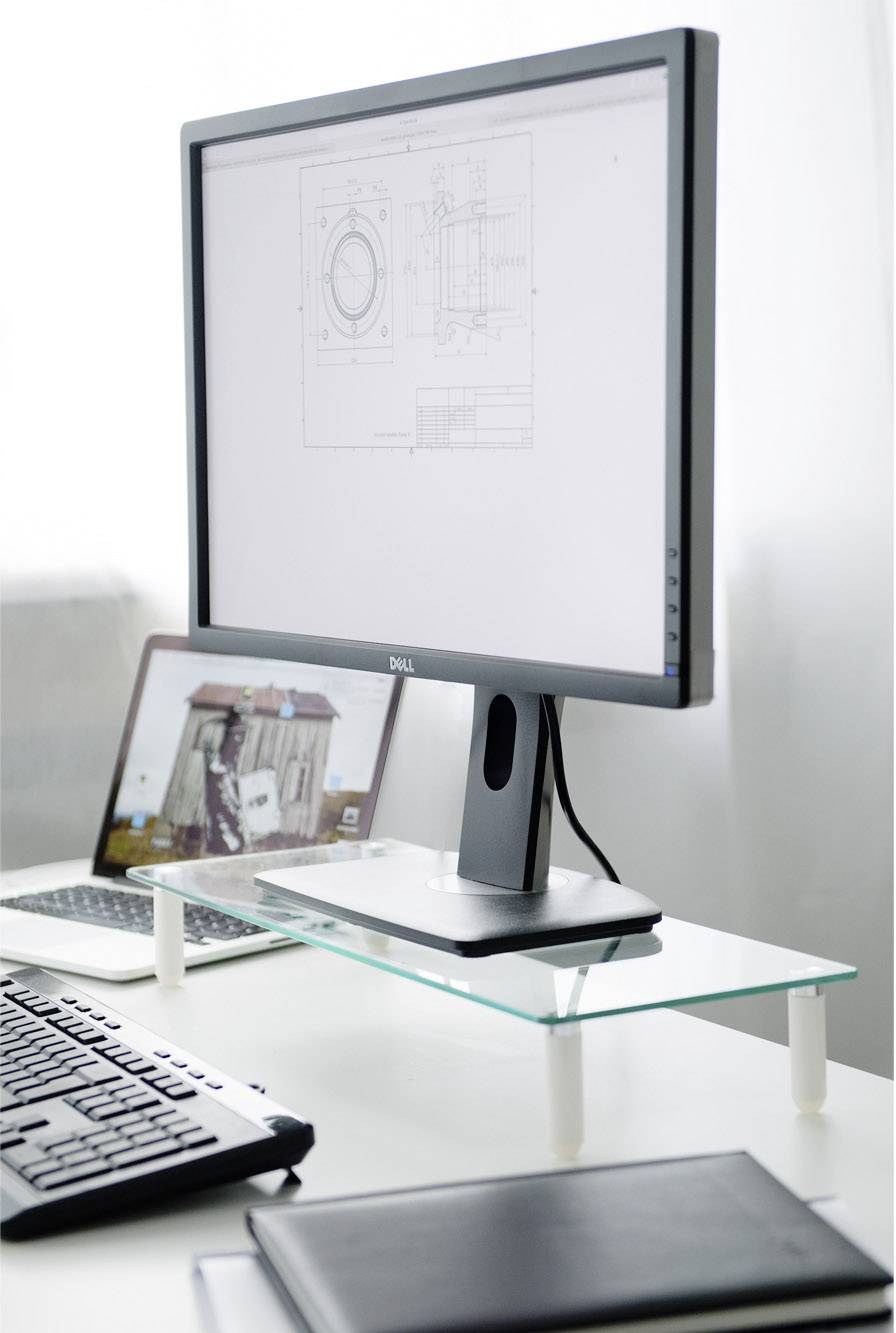 Een computerarbeidsplaats met een groot scherm waarop technische tekeningen worden getoond. Een laptop staat op de achtergrond. Toetsenbord en notitieboek liggen op tafel.