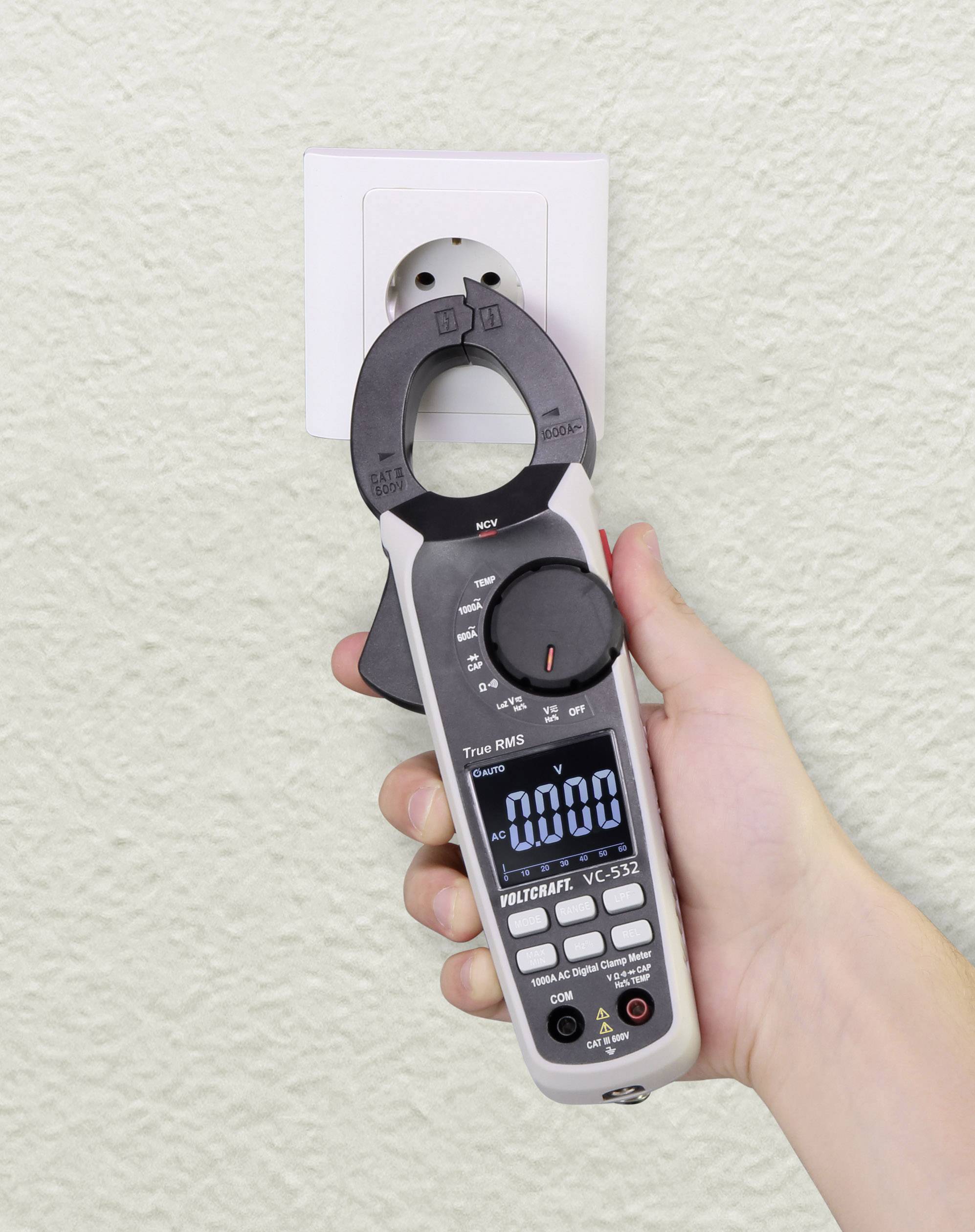 Een hand houdt een digitale multimeter naast een stopcontact, met '0,000' op het display, klaar om de spanning te meten.