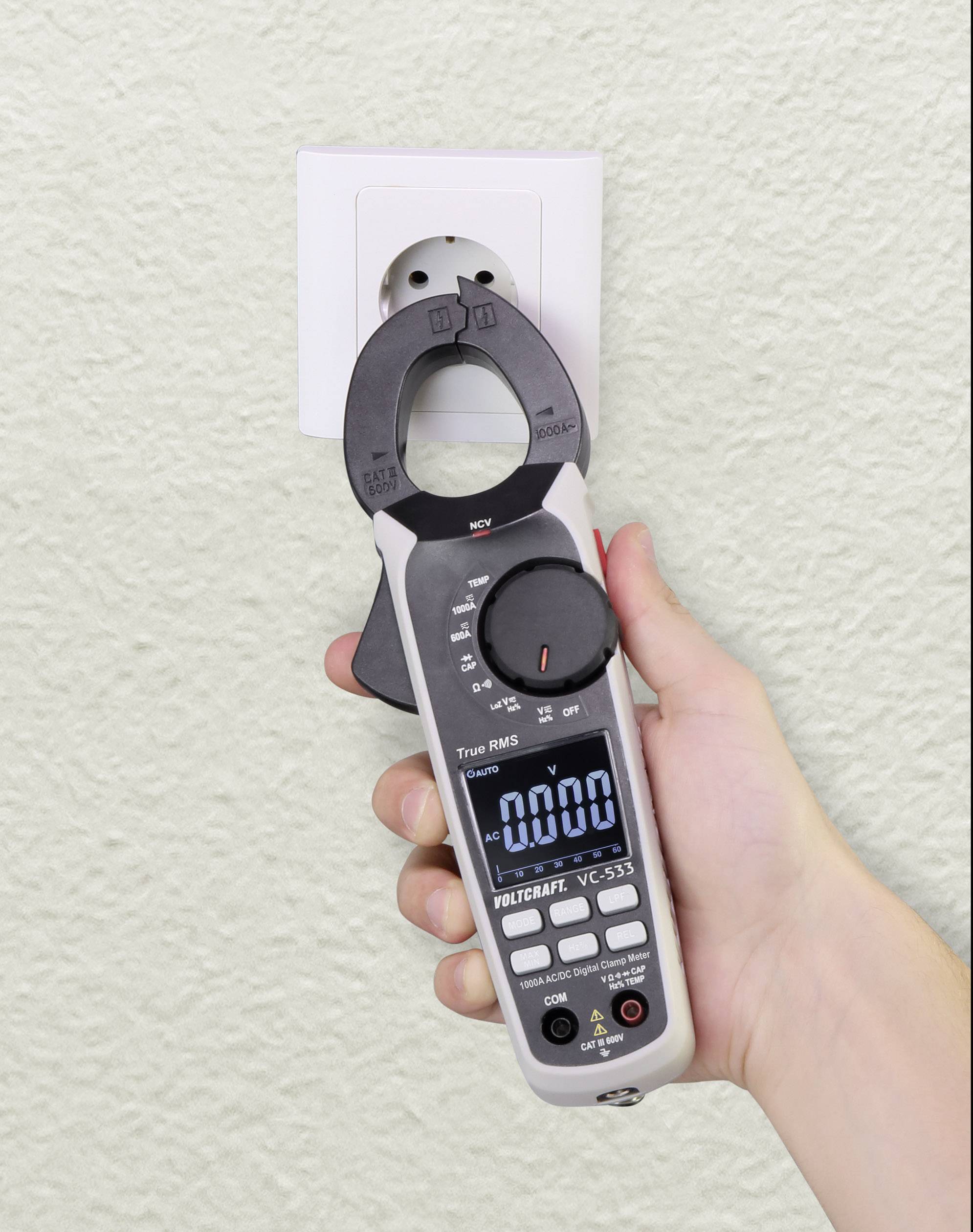 Een hand houdt een stroommetingsapparaat voor een stopcontact om elektrische waarden te controleren.