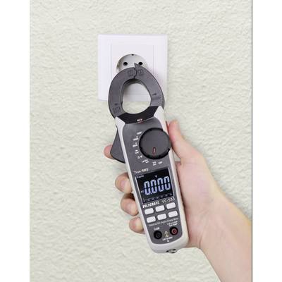 Een hand houdt een stroommetingsapparaat voor een stopcontact om elektrische waarden te controleren.