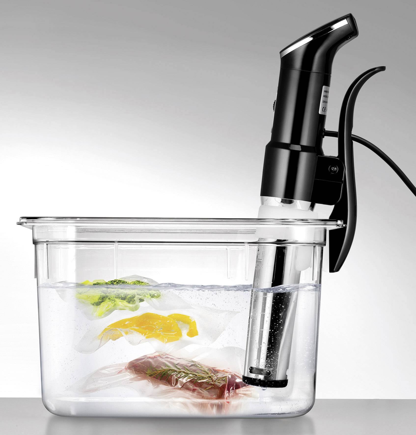 Sous-vide-kooktoestel verhit een waterbad waarin vacuüm verzegelde zakjes met groen, geel groente en vlees drijven.