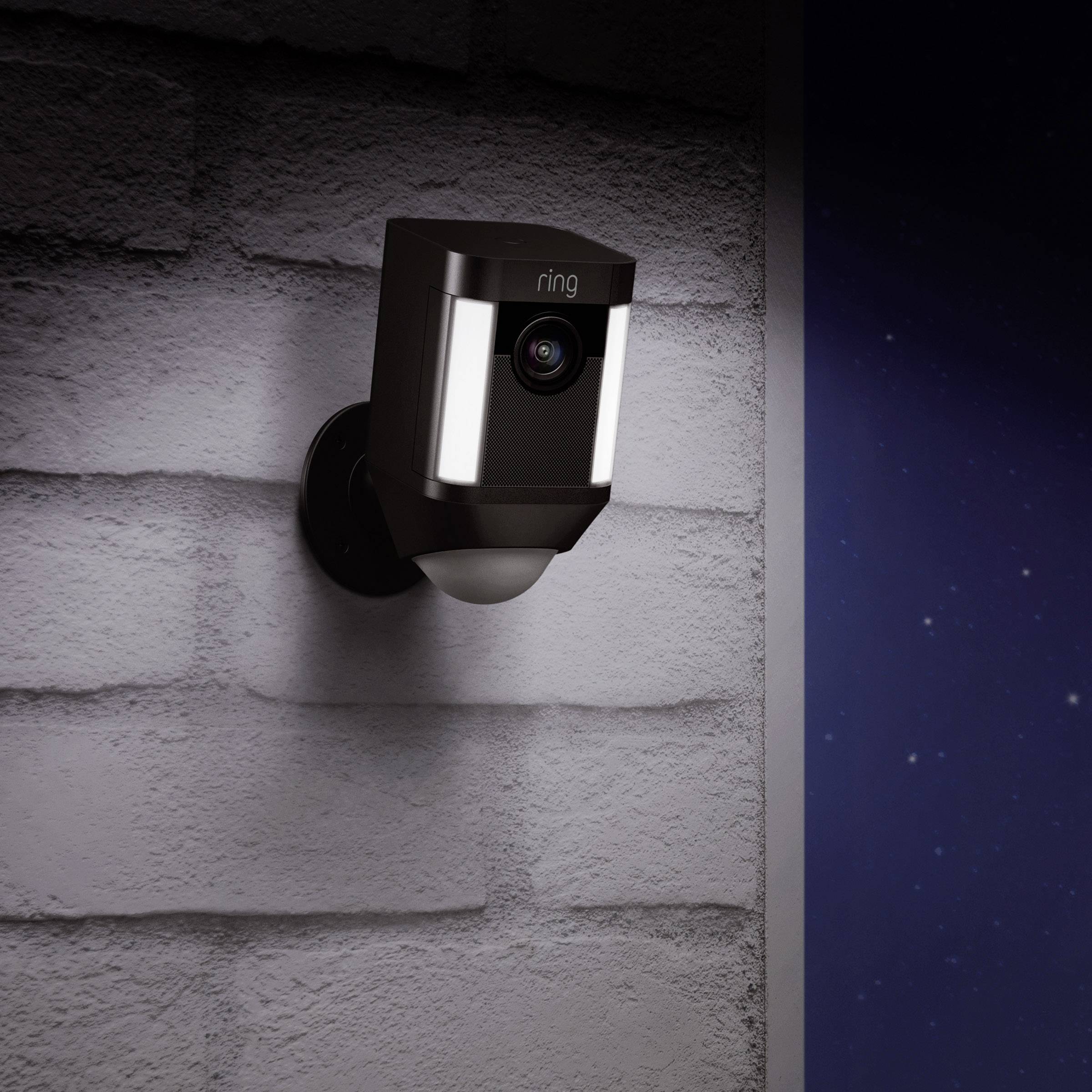 Beveiligingscamera aan een bakstenen muur, verlicht in de nacht.