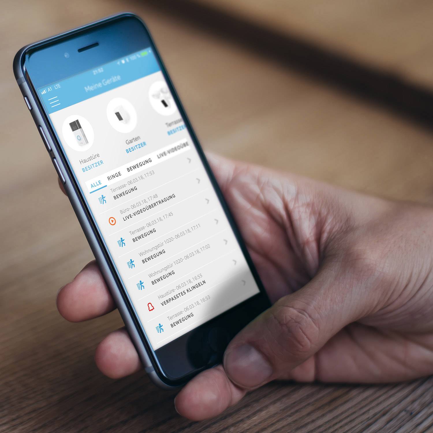Een persoon houdt een smartphone vast met een geopende app, toont een lijst met bewegingsdetecties en meldingen; de focus ligt op veiligheidstoezicht.