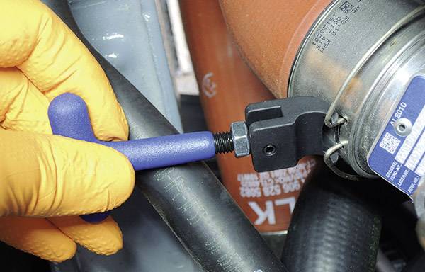 Iemand met oranje handschoenen gebruikt een blauw gereedschap om een zwarte slangklem te bevestigen aan een rode slang.