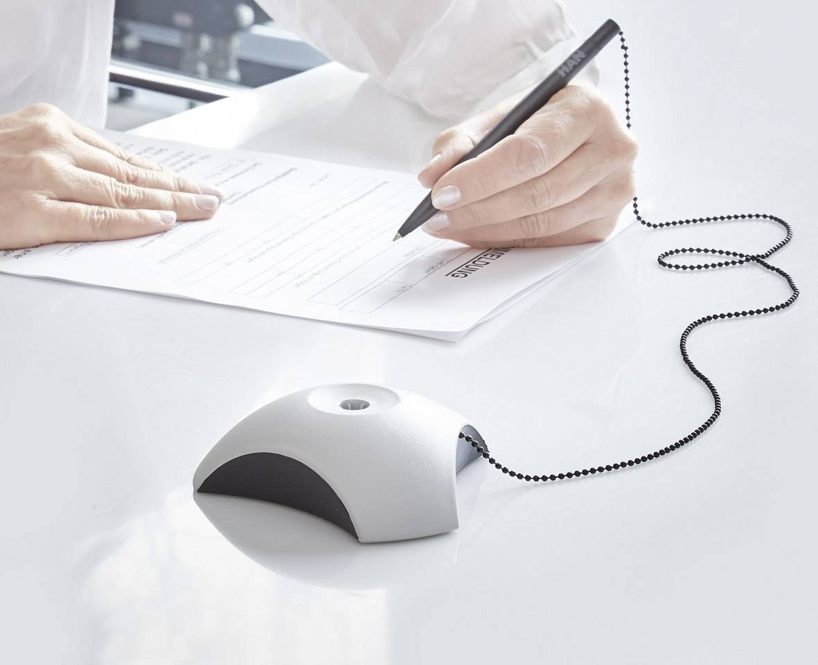 Een hand schrijft met een pen op een formulier; de pen is via een ketting verbonden met een witte houder.