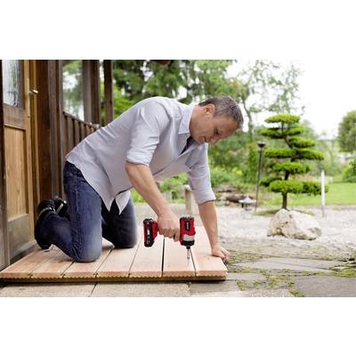 Een man knielt op een houten terras en bevestigt planken met een accuschroevendraaier. Op de achtergrond een keurig onderhouden tuin.