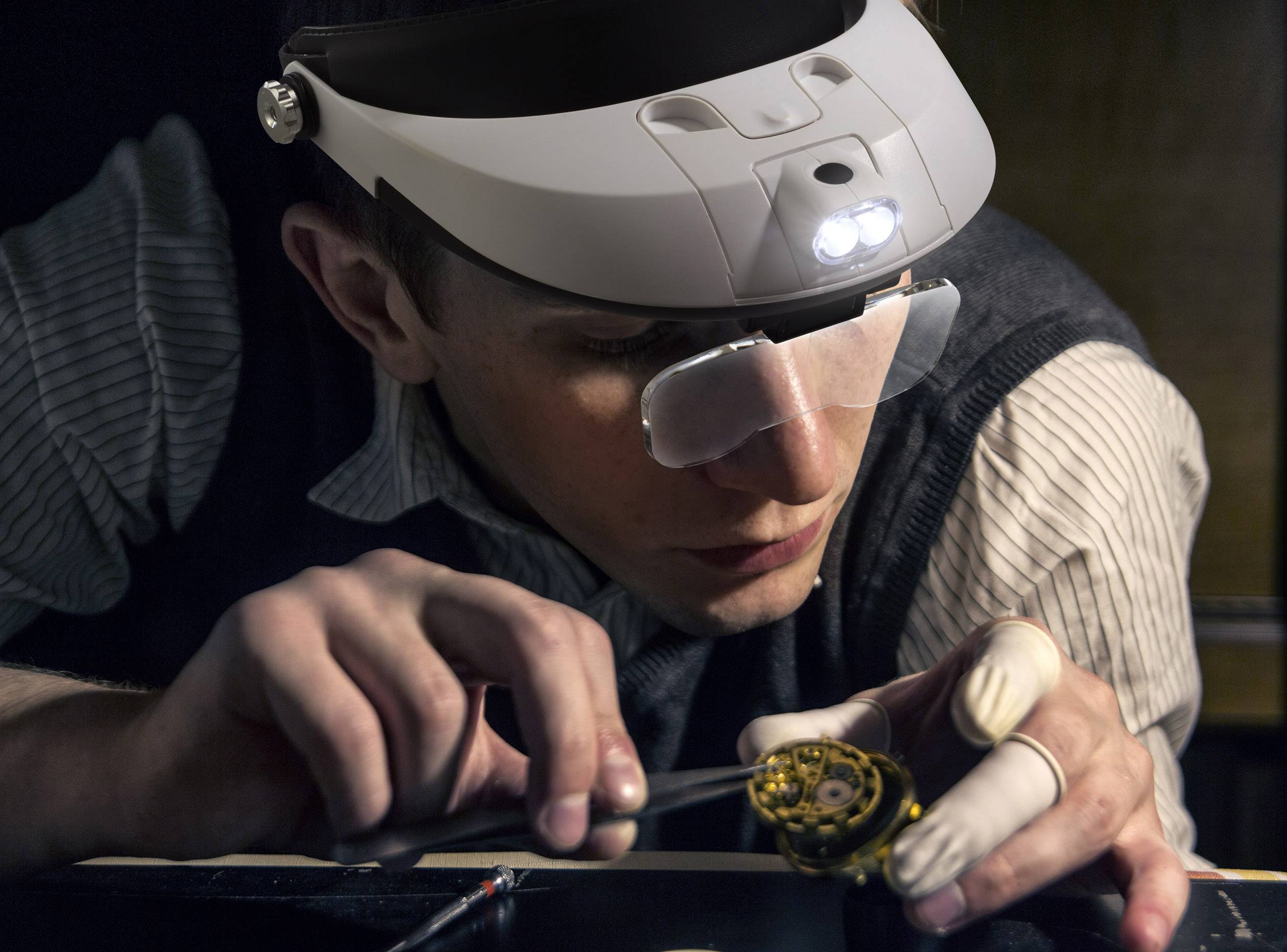 Een persoon draagt een koploep met licht en repareert een horloge met een fijn gereedschap, geconcentreerd op de horlogeonderdelen.