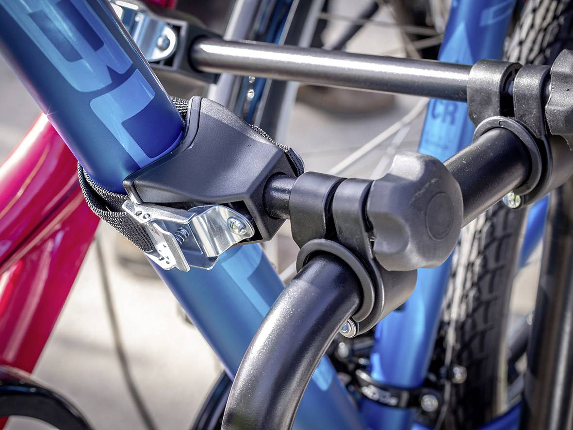 Close-up van een blauw gelakt fietsframe in een stevig veiligheidsslot. Op de achtergrond is een rood fietskader zichtbaar.