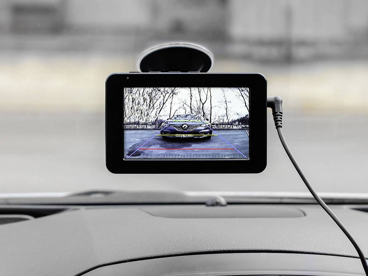 Een achteruitrijcamera-display toont een zwarte sportwagen achter het voertuig. Dient ter ondersteuning bij het achteruit rijden.