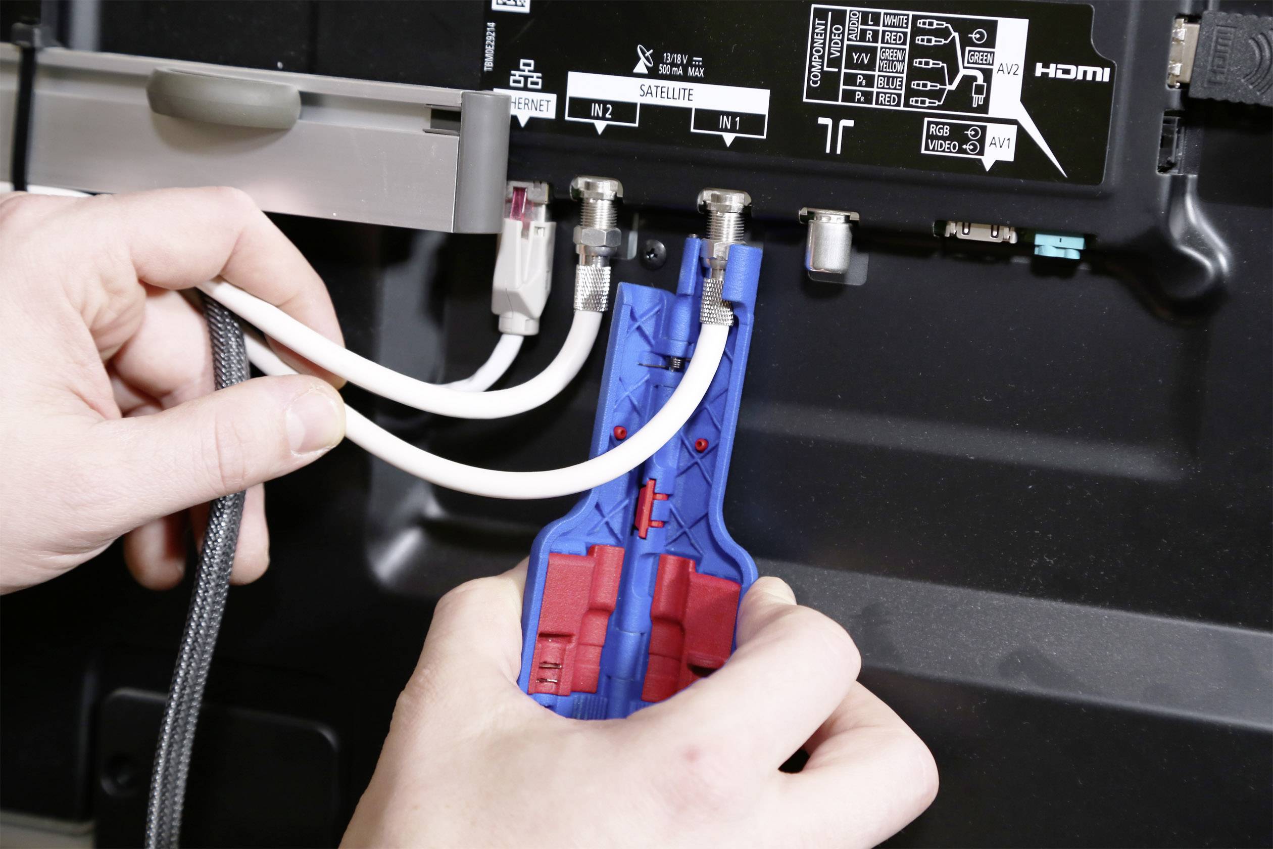 Een persoon gebruikt een kabeltest-apparaat om coaxkabels aan de achterkant van een elektronisch apparaat te testen.