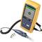 Een geel elektronisch testapparaat met een scherm toont 'PASS'. Ernaast liggen een optische sonde en vier kleine accessoireonderdelen.