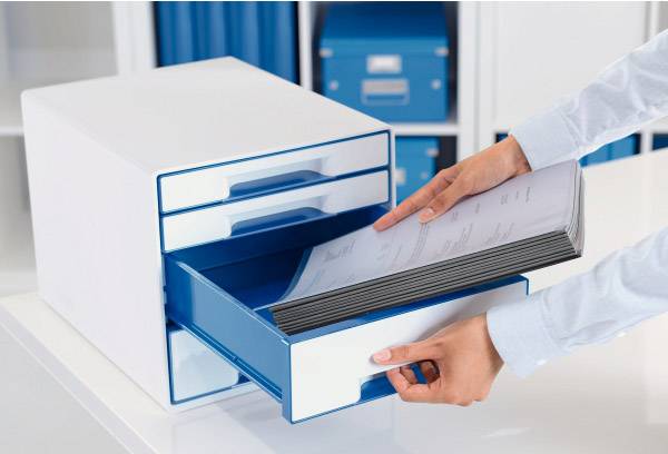 Een persoon legt papierstapels in een geopende lade van een blauw en wit archiveringsysteem op kantoor.