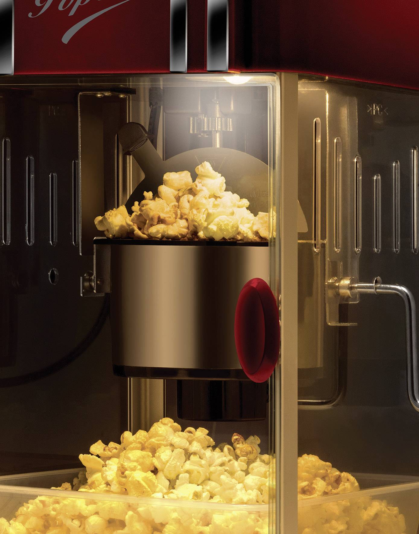 Popcornmachine met verse popcorn, zichtbaar door een glazen venster. Popcorn valt uit een metalen container naar het onderste gedeelte.