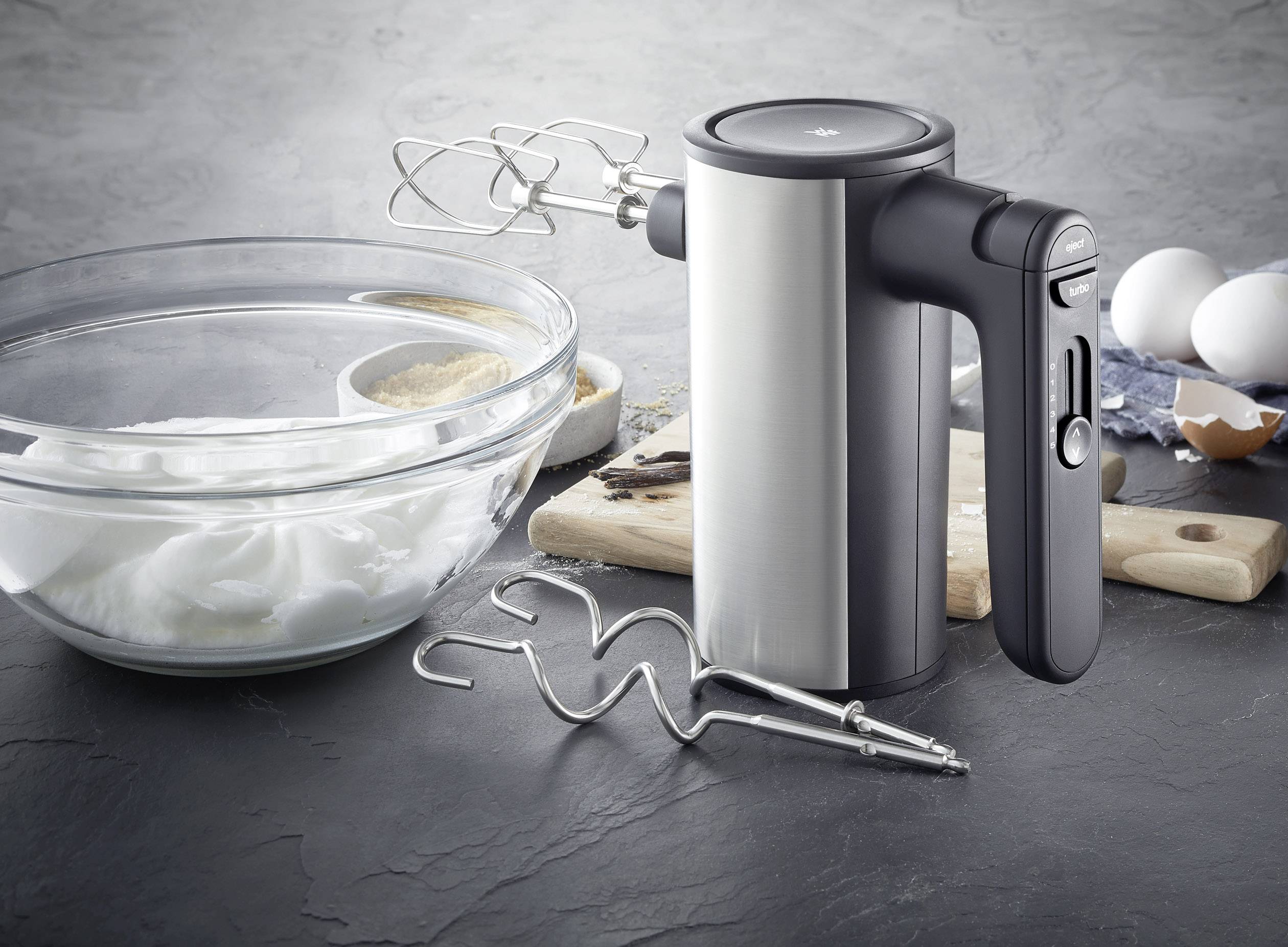 Een elektrische handmixer staat op een aanrechtblad met garden, ernaast een kom met geslagen eiwit.