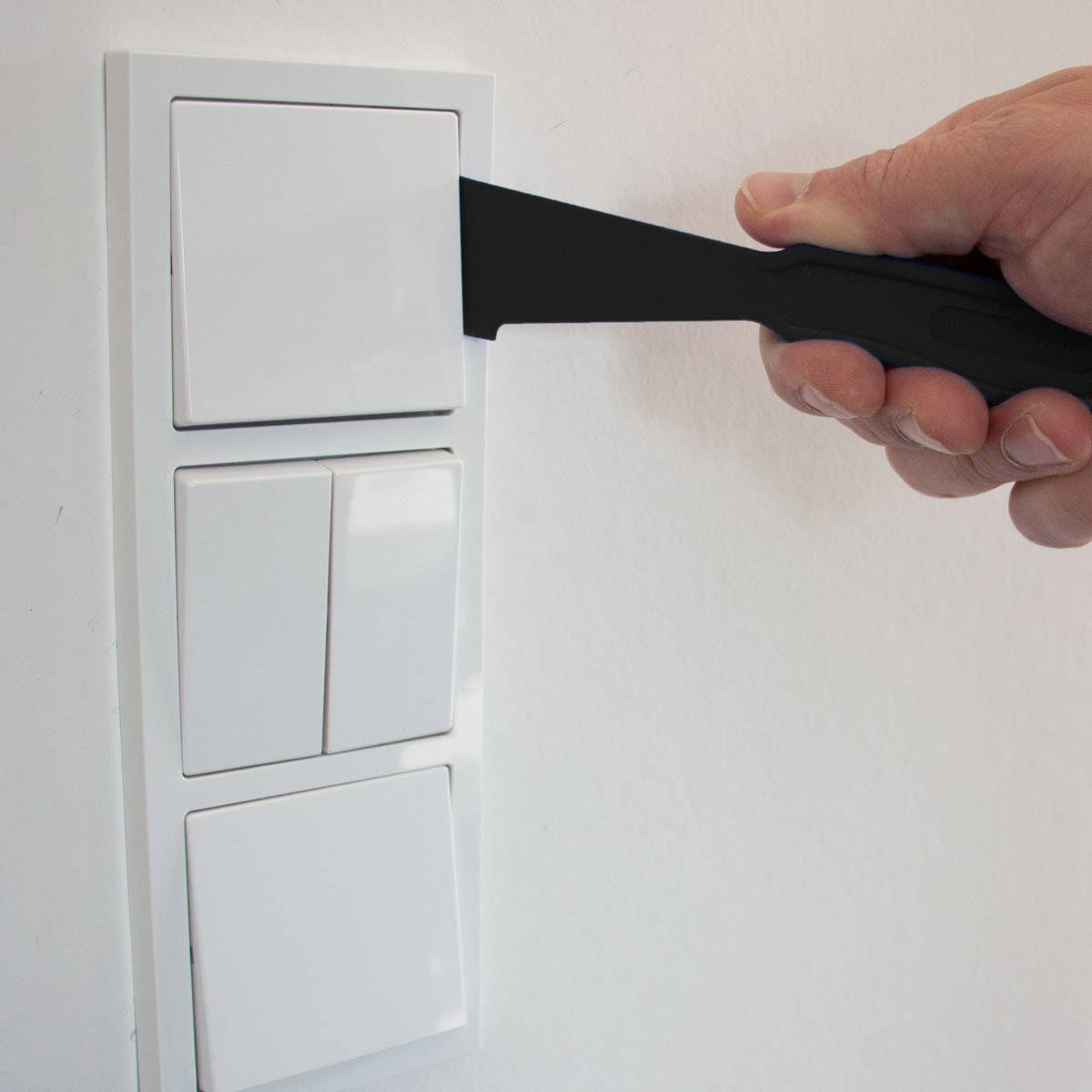 Een hand houdt een groot mes vast dat tussen een dubbele lichtschakelaar steekt.