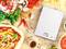 Digitale keukenweegschaal op een houten tafel, omringd door verse pizza-ingrediënten zoals deeg, groenten, kruiden en specerijen. Display toont '0'.