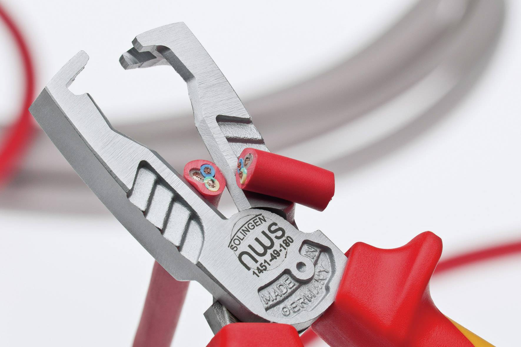 Een tang knipt een rood kabel door. Men ziet de draadaders in de kabel. Op de achtergrond zijn meer kabels zichtbaar.