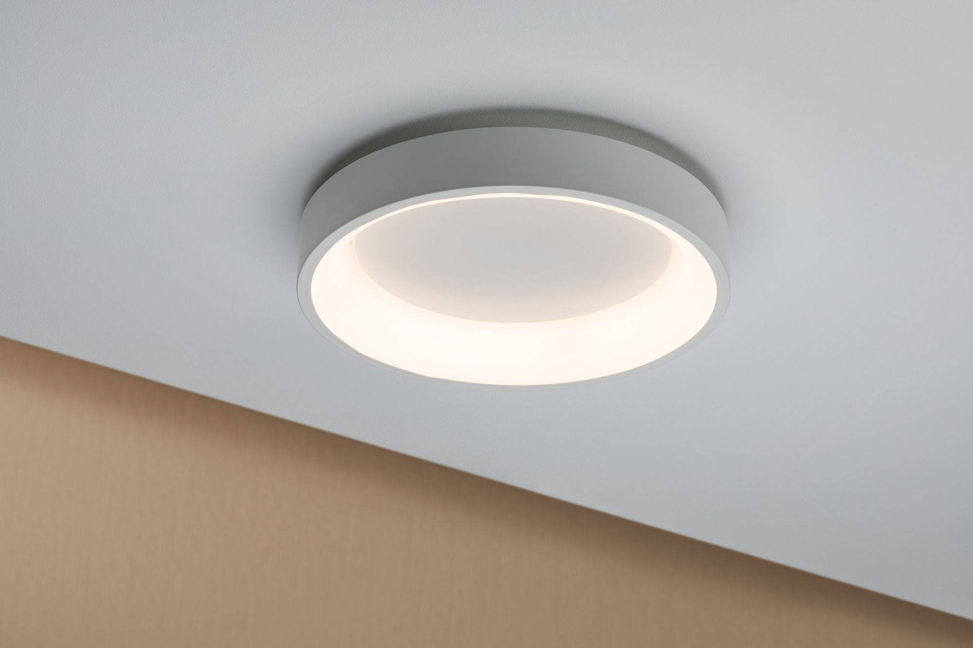 Een rond, modern plafondlicht met verlichtende LED-ring op een beige plafond, zorgt voor een gelijkmatige ruimteverlichting.