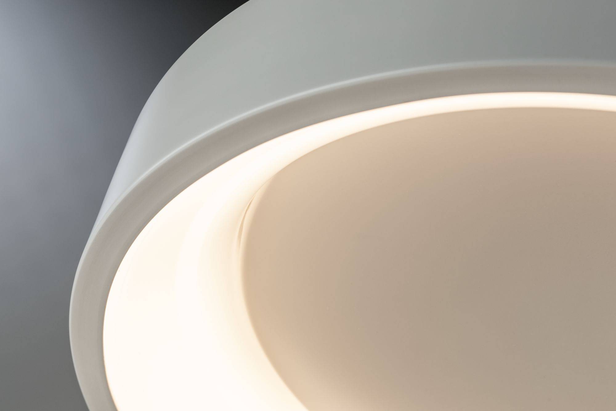 Close-up van een moderne, ronde plafondlamp met zachte, warme verlichting. De lamp heeft een eenvoudig, elegant design.