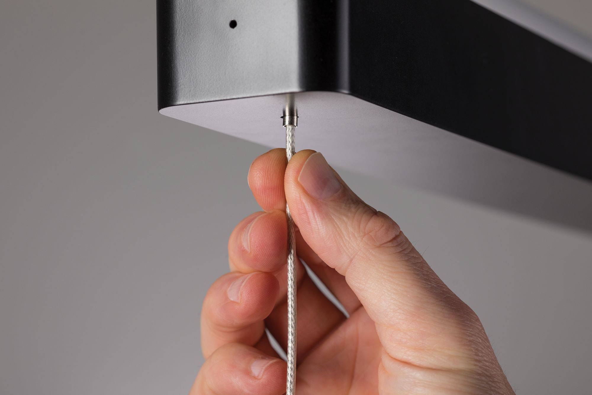 Een hand trekt aan een touw dat bevestigd is aan een zwart rechthoekig object, mogelijk een lamp of apparaat.