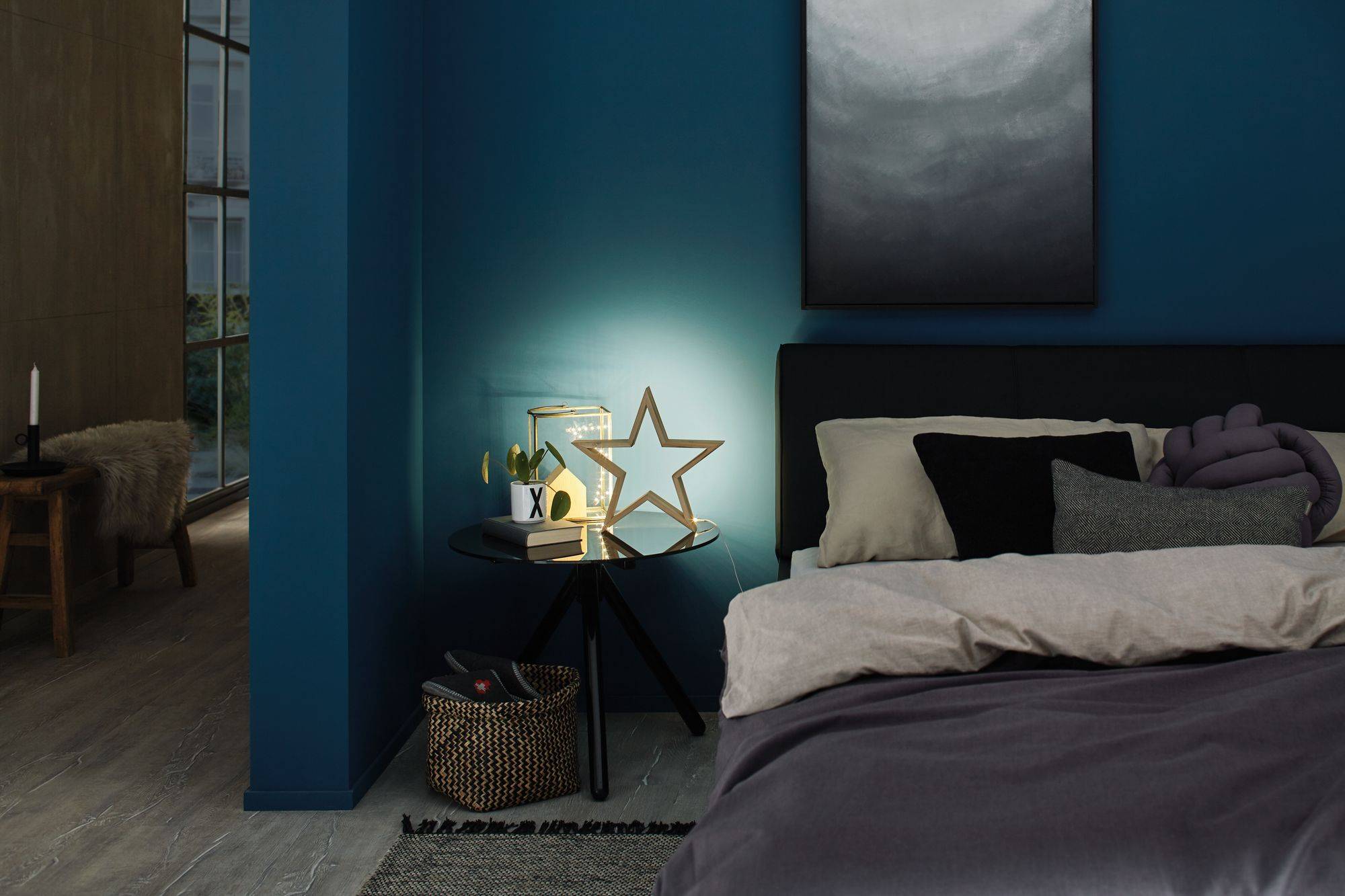 Slaapkamer met blauw geschilderde muur, modern bed met kussens, nachtkastje met sterrenlamp en decoratie.