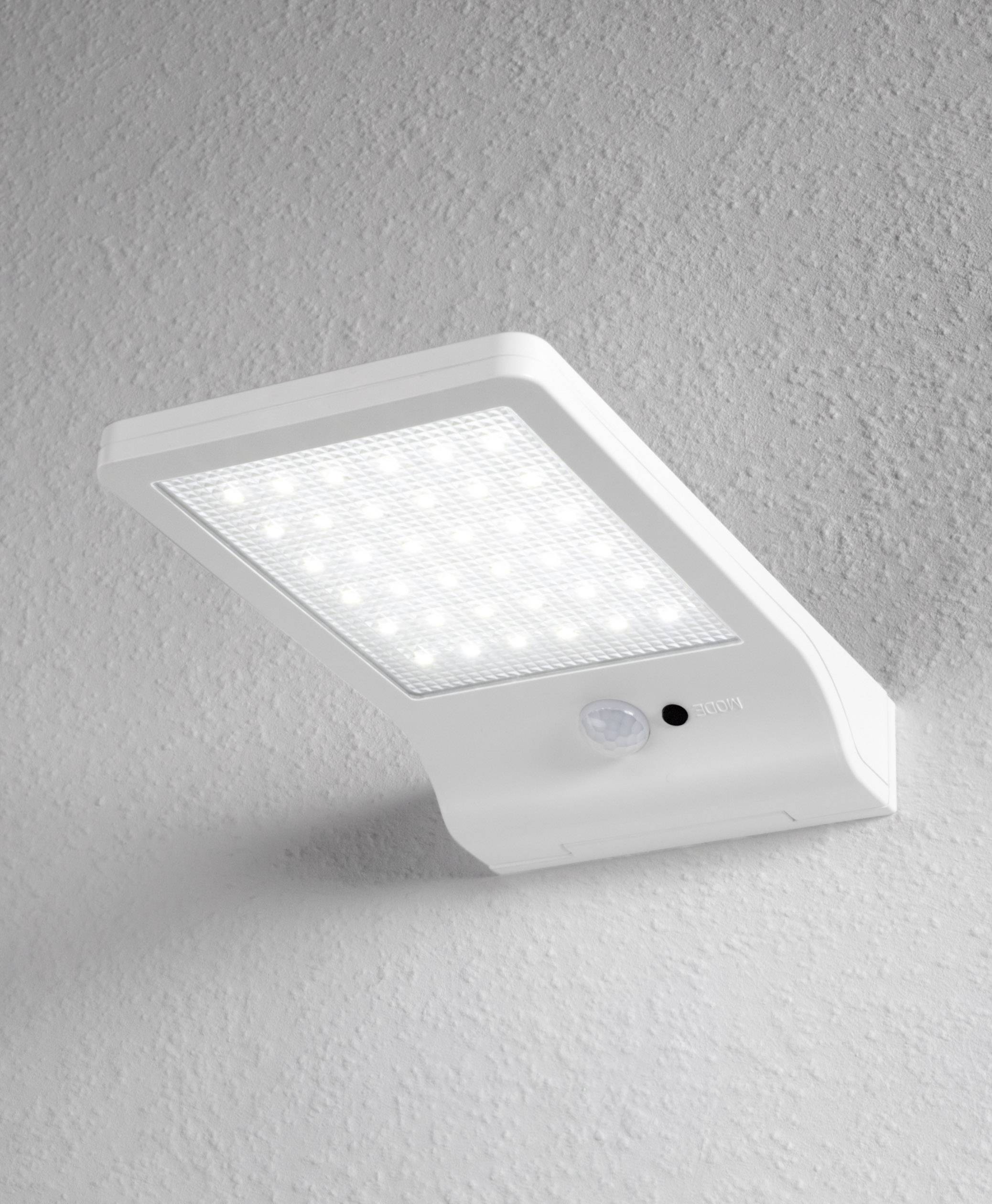 Witte LED-wandlamp met bewegingssensor gemonteerd aan een grijze muur, toont rechthoekig verlichtingsoppervlak. Ideaal voor buitenruimtes.