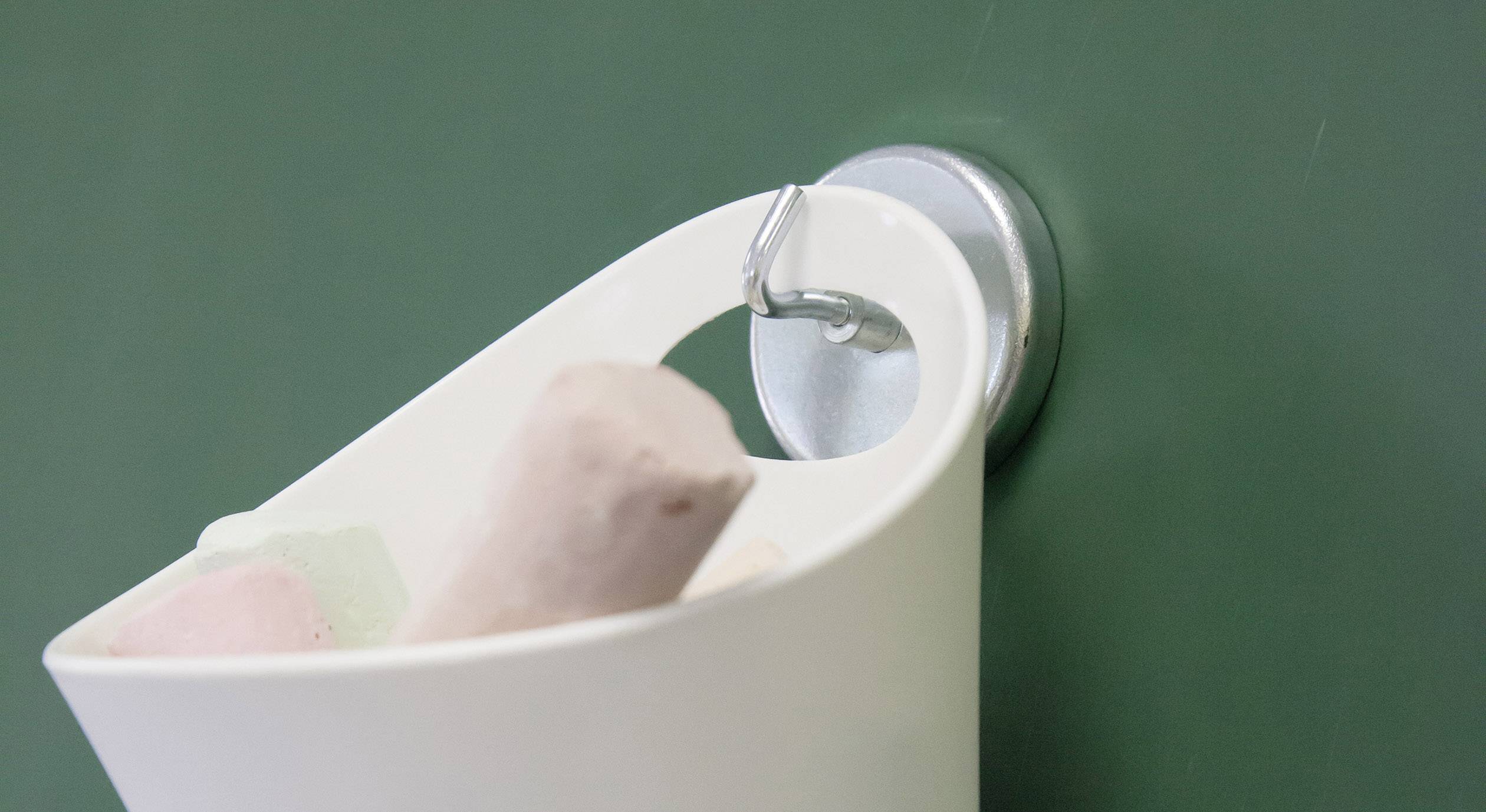 Een kleine witte emmer met gekleurde krijtjes hangt aan een haak voor een groen schoolbord.