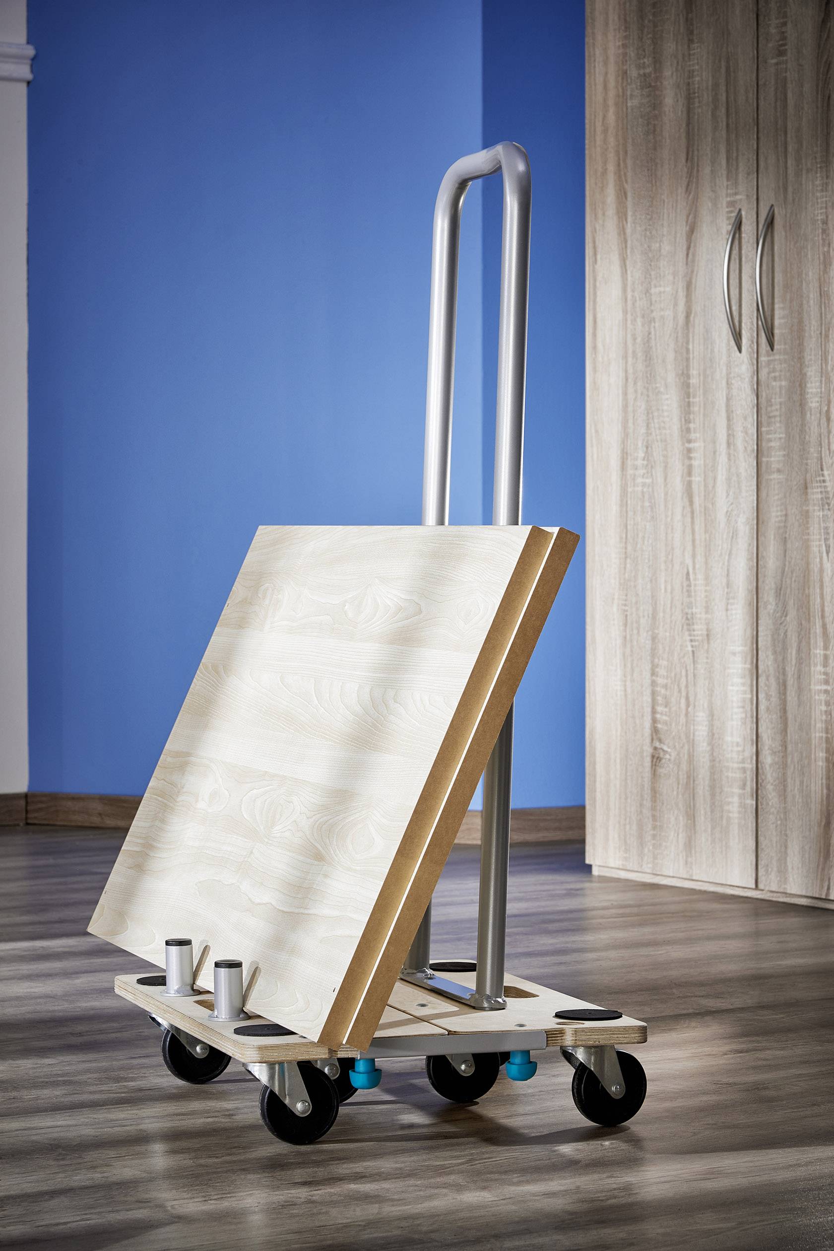 Een transportwagen met twee houten platen staat op een houten vloer. Op de achtergrond is een blauw wandgedeelte en een houten kast te zien.