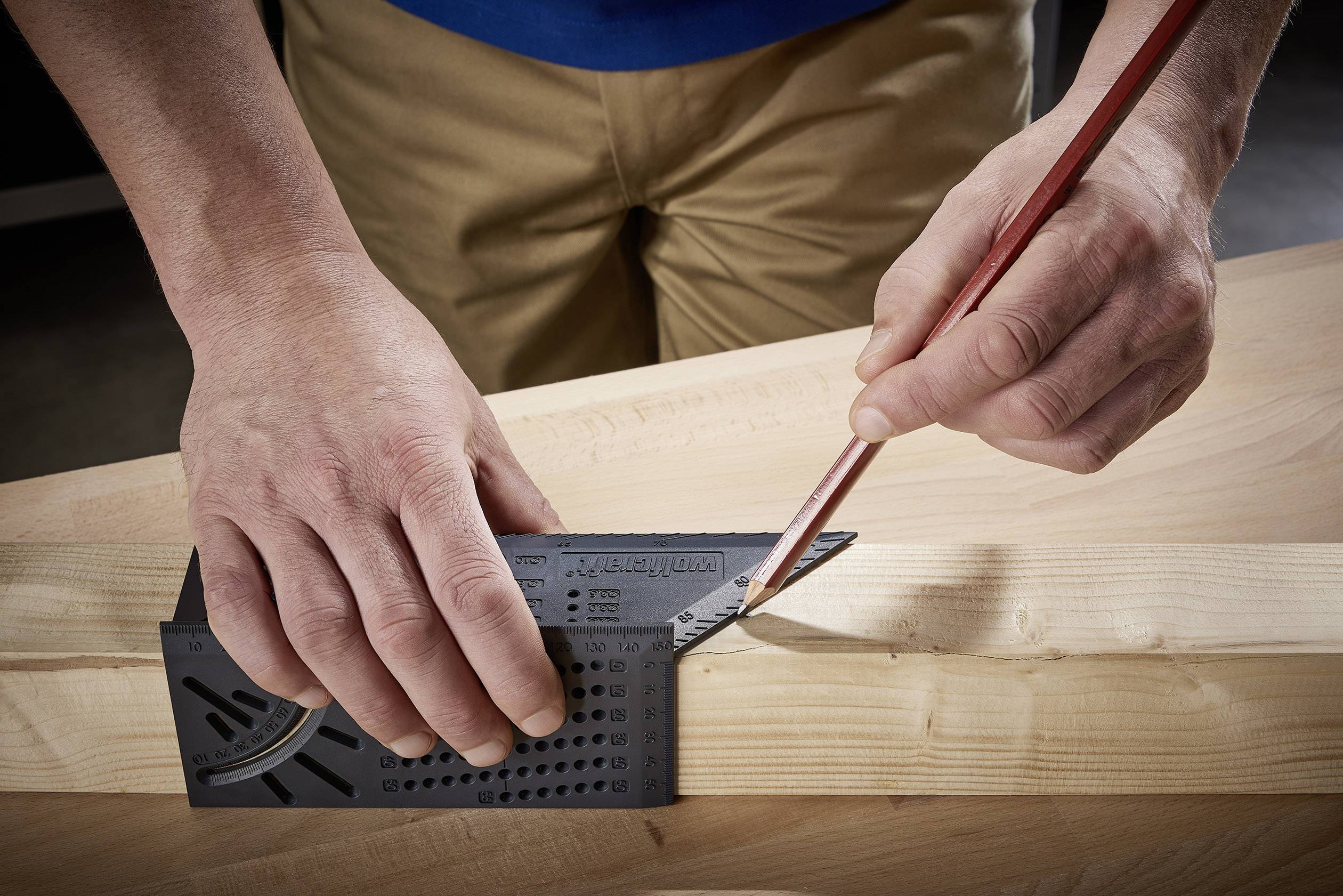 Een persoon meet met een gradenboog de positie op een stuk hout en markeert een lijn met een potlood.