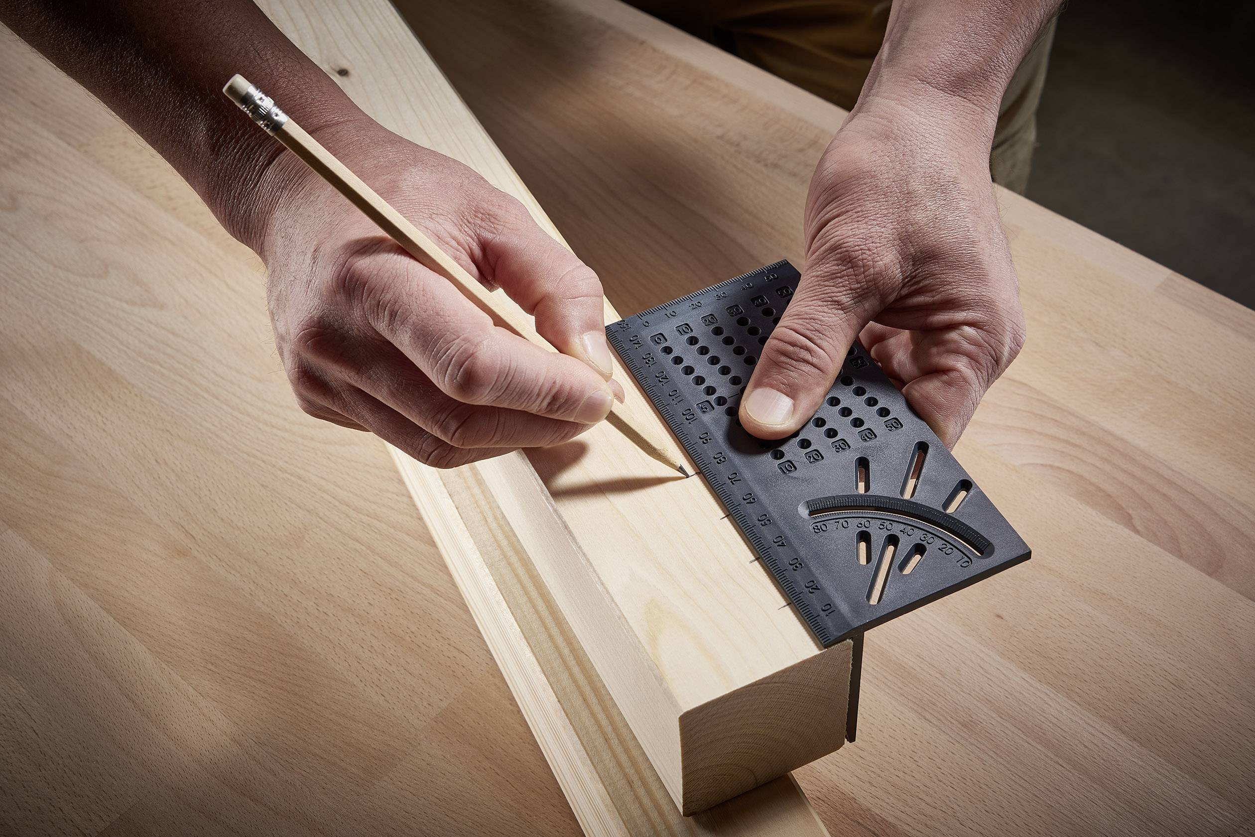 Een persoon tekent met een potlood en een gradenboog nauwkeurig lijnen op een stuk hout.