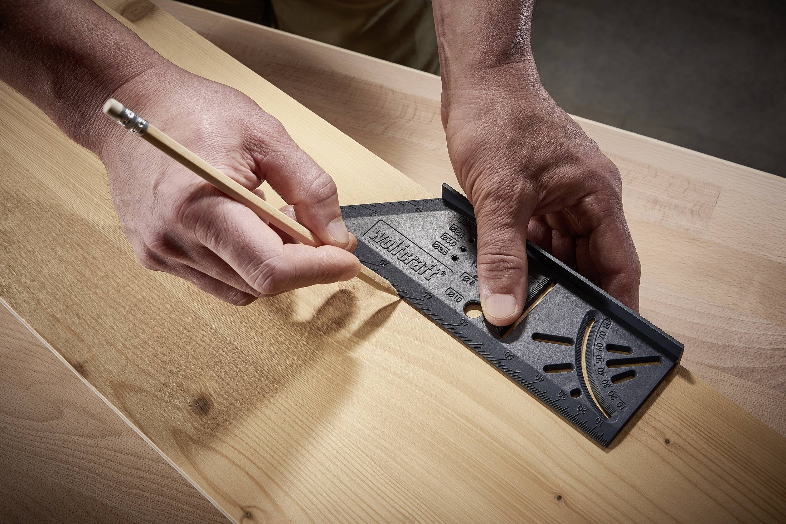 Een persoon tekent met een potlood en een timmermanshaak een lijn op een stuk hout.