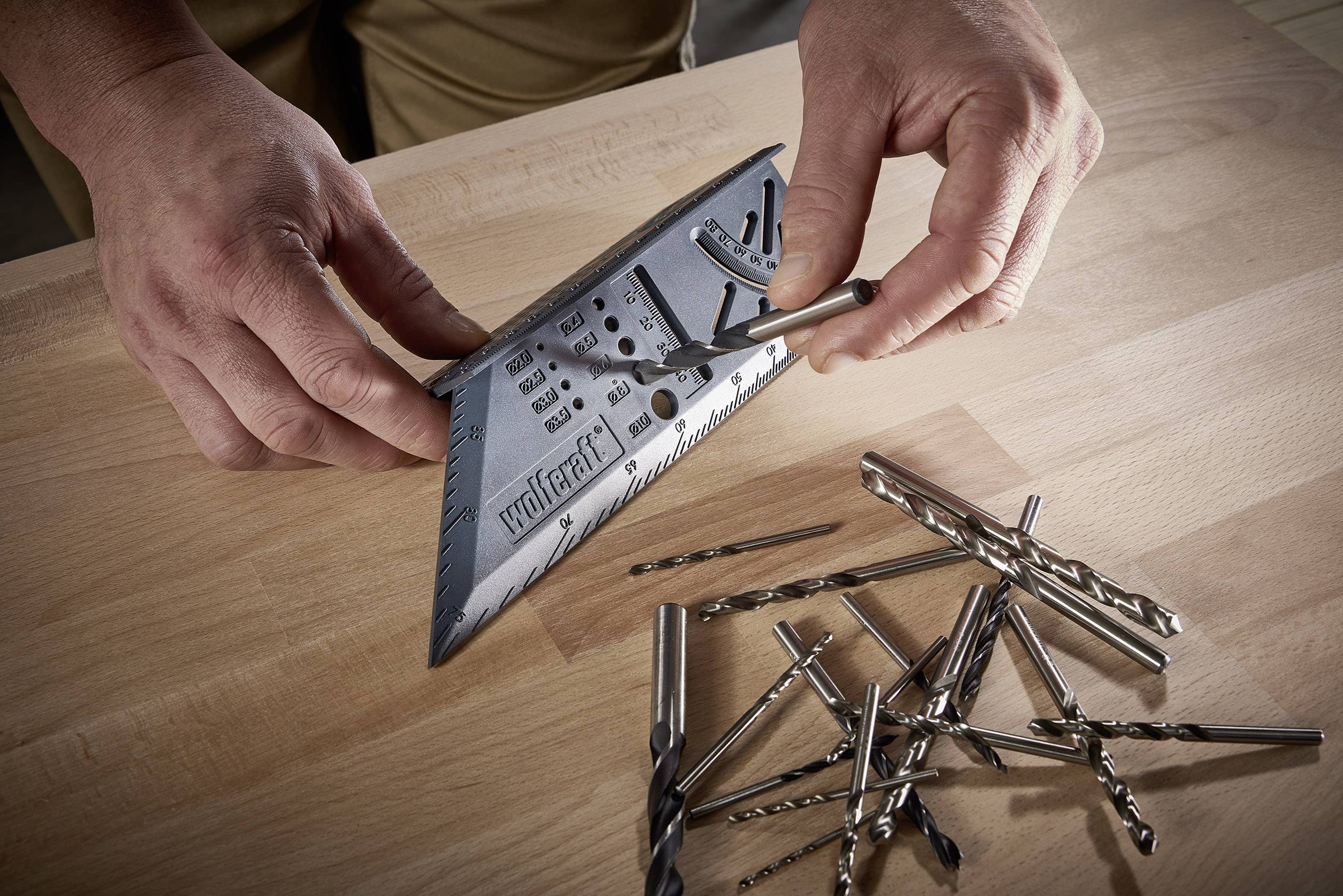 Een persoon meet een boor met een gradenboog, omringd door verschillende boren op een houten tafel.