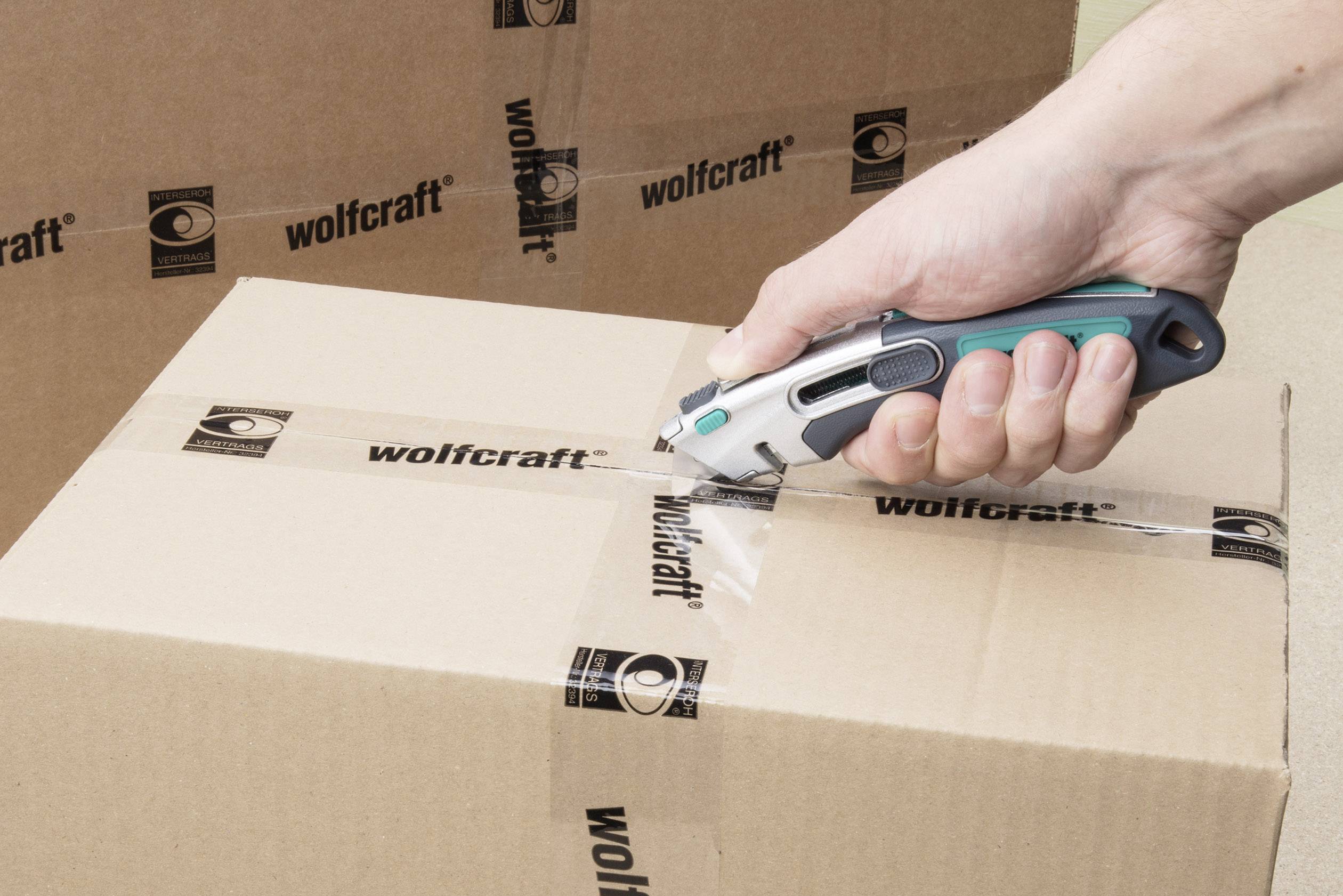 Een hand gebruikt een stanleymes om plakband van een kartonnen doos met het 'wolfcraft'-logo door te snijden.