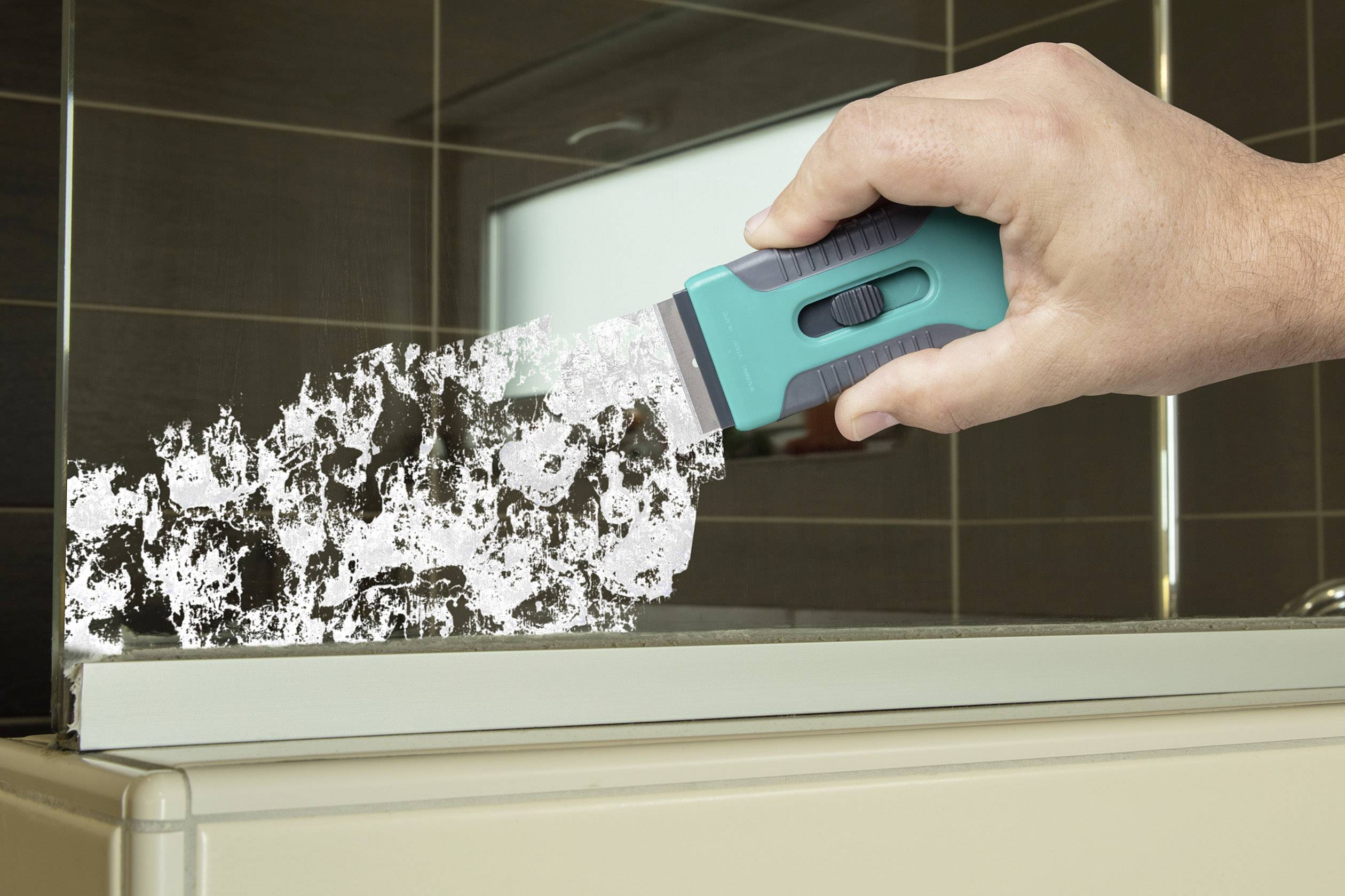 Een hand houdt een groene schraper vast en verwijdert hardnekkig vuil van een glazen oppervlak in een badkamer.