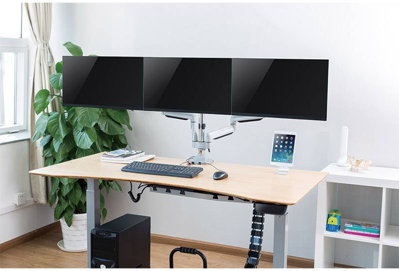 Een bureau met drie grote monitoren, toetsenbord, muis en tablet. De monitoren zijn naast elkaar gemonteerd op een monitorarm.